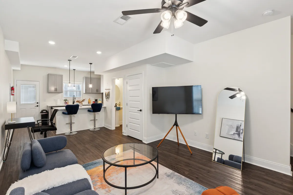 The image captures a cozy living space with a comfortable sofa, sleek coffee table, a television, and a decorative mirror. The seating arrangement encourages both relaxation and social gatherings, while the soft lighting maintains a warm, inviting ambiance.