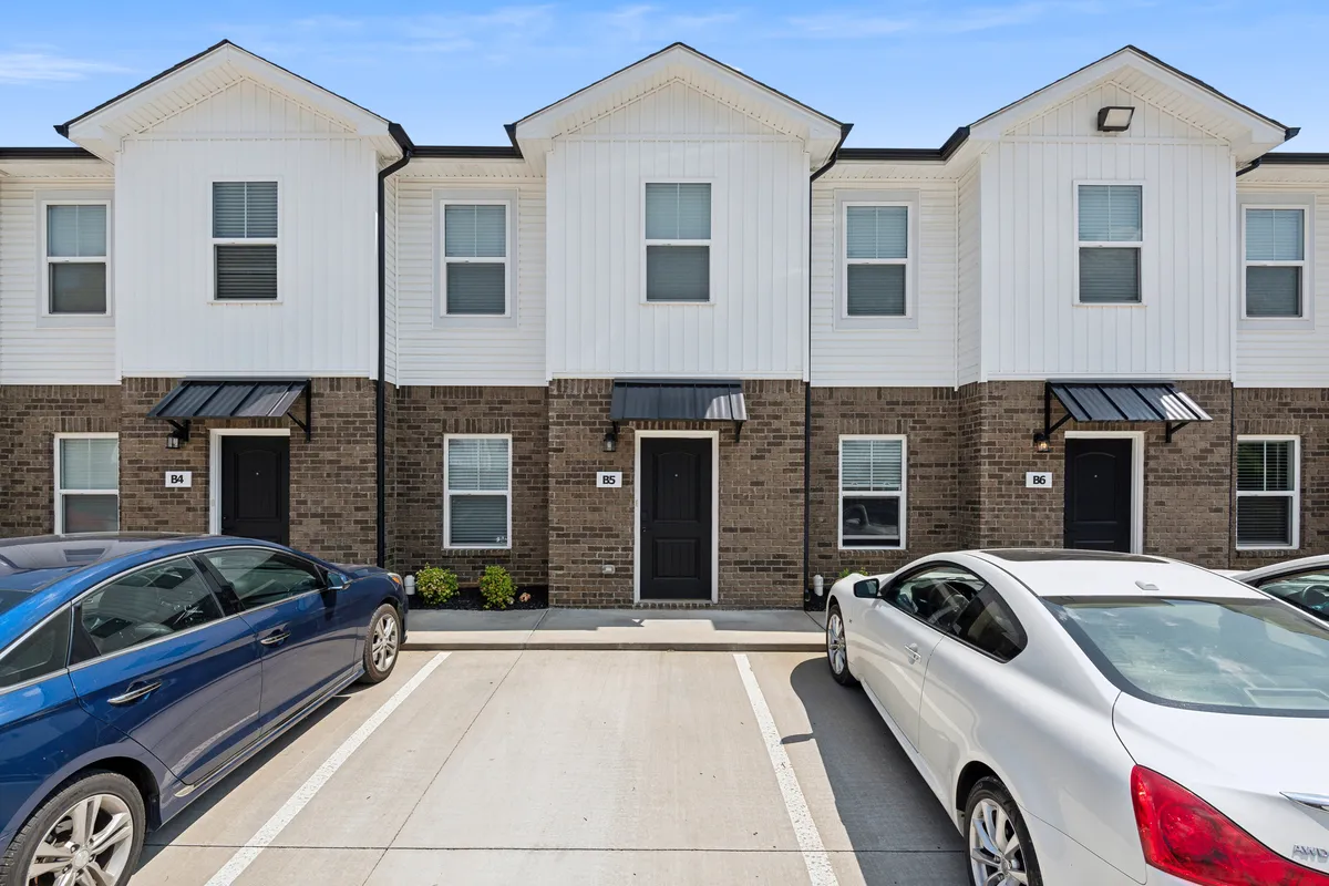 A friendly, inviting view of the townhouse-style property, featuring clearly visible parking arrangements, front doors, and a charming residential facade. The scene conveys a sense of arrival and ease for guests.