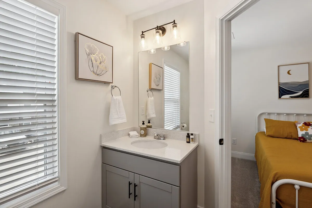 A vanity area with a modern sink and mirror, complemented by neatly folded towels and stylish framed artwork. The view toward the bedroom doorway offers a glimpse into the suite’s layout, highlighting spaces for personal care and relaxation.