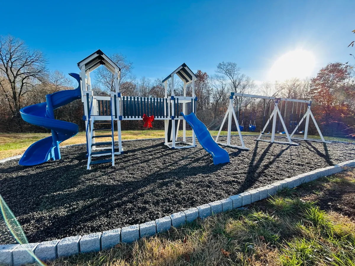 This exterior image captures a vibrant playground with a blue slide, swings, and children actively playing. The scene is energetic and inviting, reflecting a welcoming local park atmosphere ideal for families and groups.