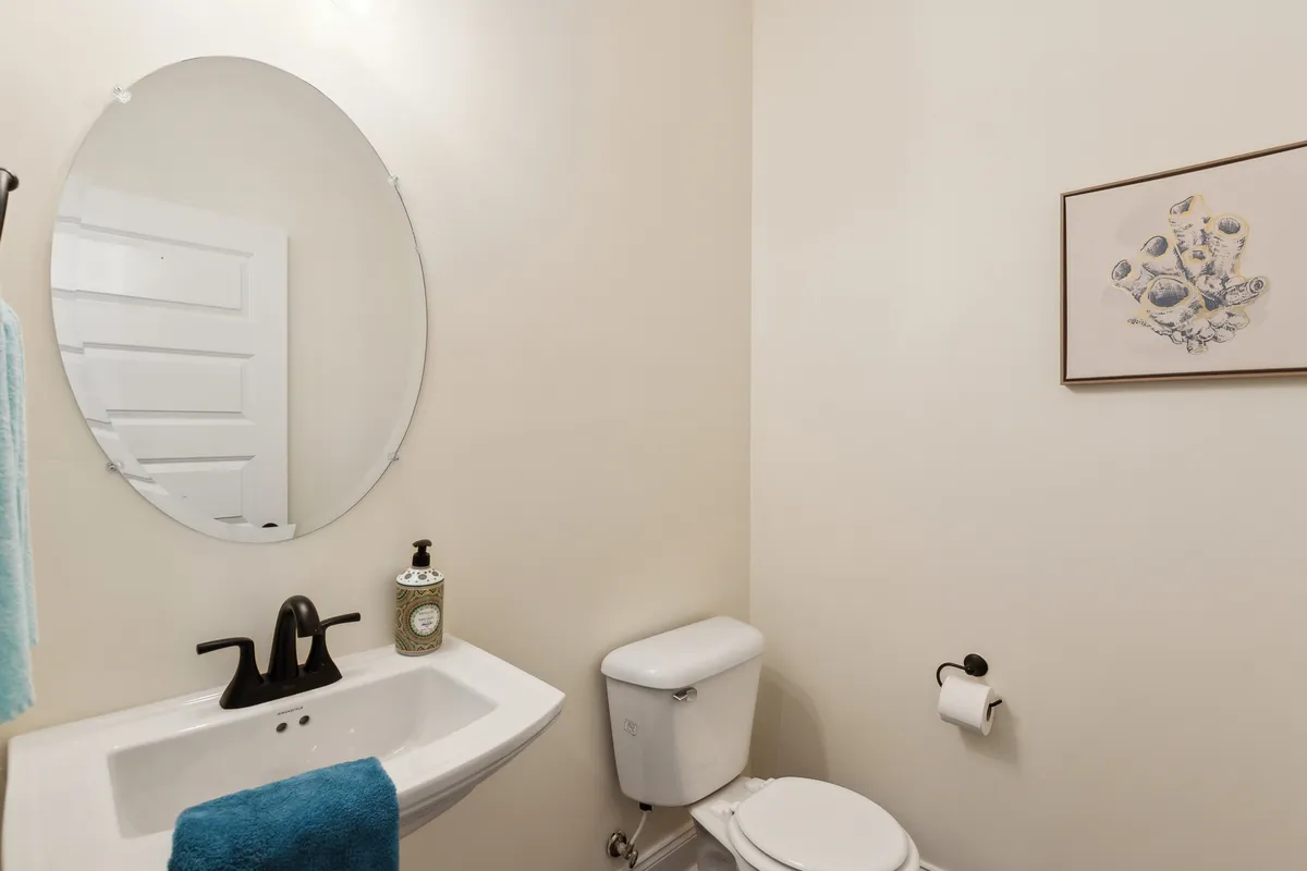 A refreshing bathroom with an oval mirror above the sink, a toilet, and framed artwork. The space is styled for personal grooming and self-care, with towels neatly arranged for convenience. The atmosphere is serene and inviting.