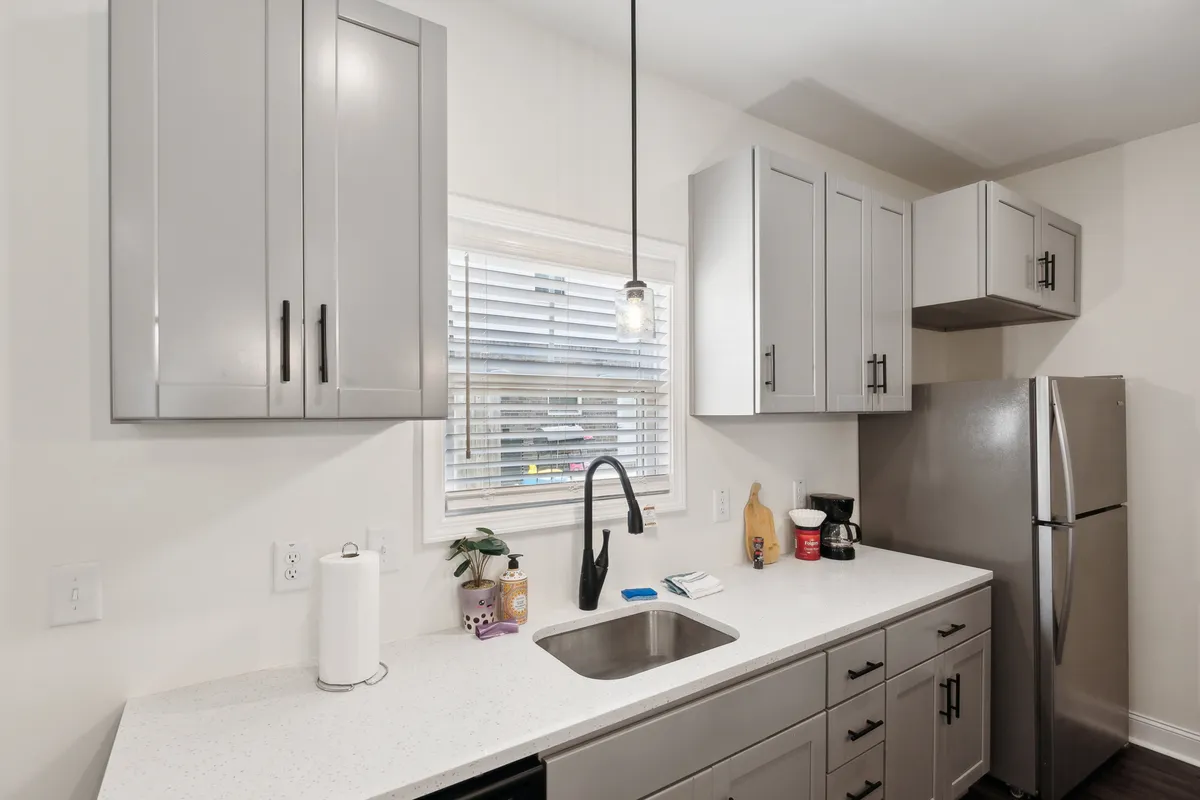 A functional and welcoming kitchen scene featuring a sink, ample countertop space, a window for natural light, and modern appliances. The layout invites both cooking and gathering, evoking the idea of shared meal preparation and enjoyment.