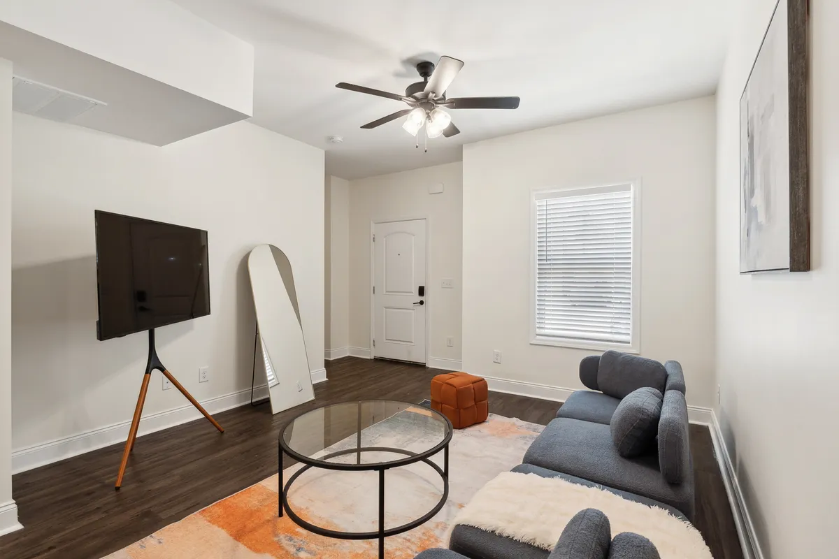 A cozy living room set up with a comfortable sofa, coffee table, television, and a view of the front door, all set in a warm, inviting atmosphere. The open layout suggests easy movement and accessibility throughout the apartment.